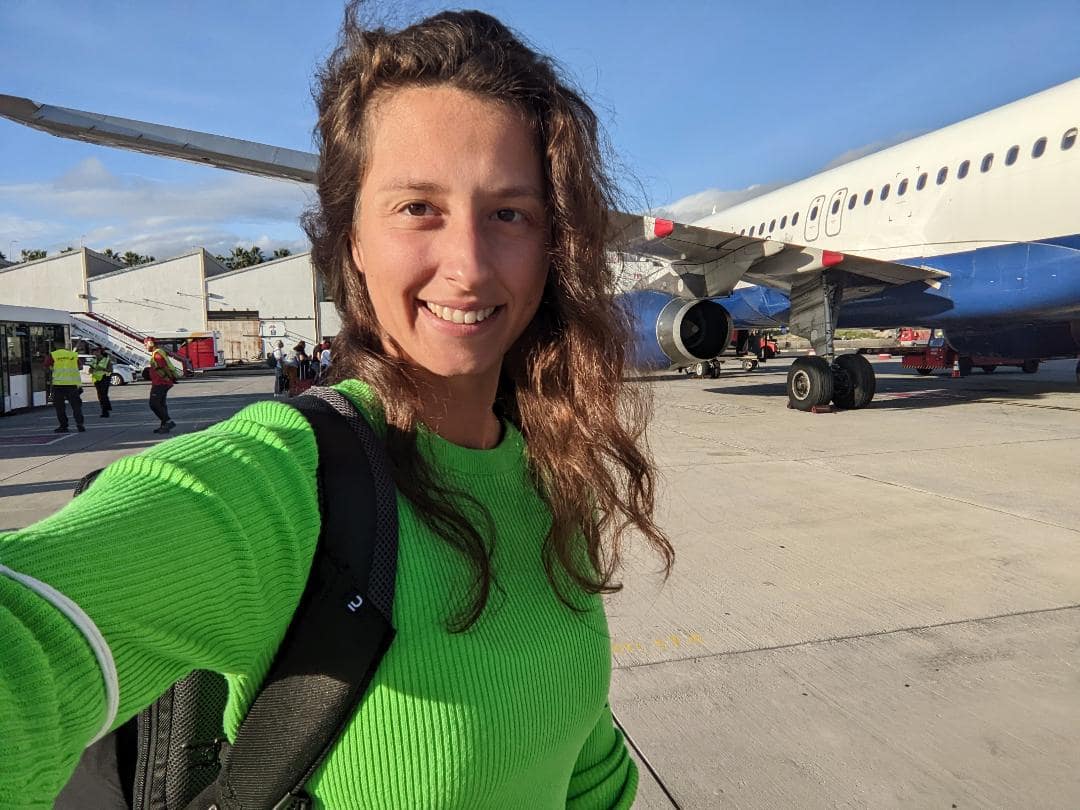 Dievča v žltom tričku sa fotí na letisku s lietadlom.