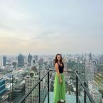 Dievča stojace na streche mrakodrapu v Bangkoku. Za ňou sa rozlieha veľké mesto.