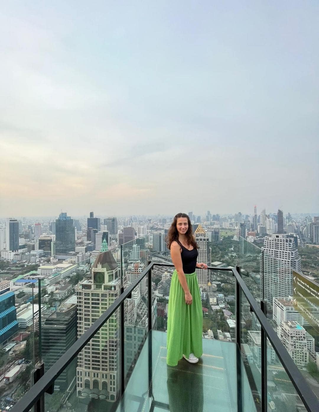 Dievča stojace na streche mrakodrapu v Bangkoku. Za ňou sa rozlieha veľké mesto.