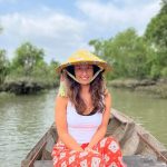Dievča s tradičným vietnamským klobúkom sedí na drevenom člne uprostred rieky Mekong.