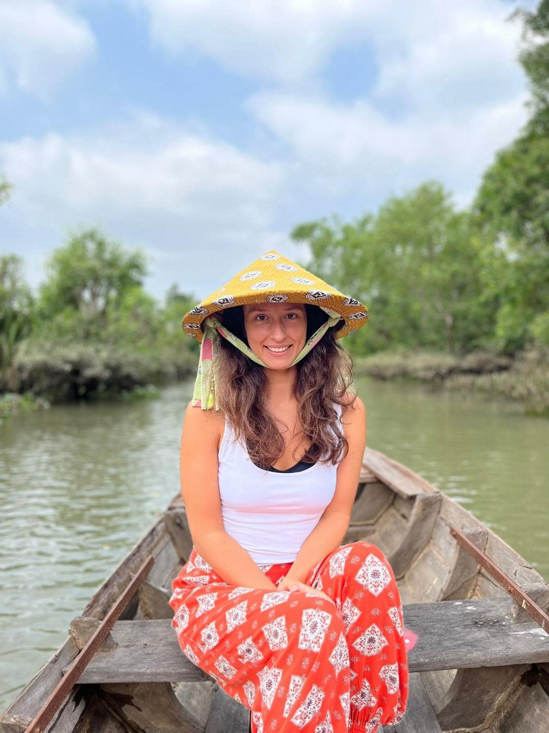 Dievča s tradičným vietnamským klobúkom sedí na drevenom člne uprostred rieky Mekong.