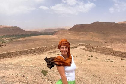 Usmiate dievča uprostred marockej púšte. Je zahalená v šatke a fúka vietor.