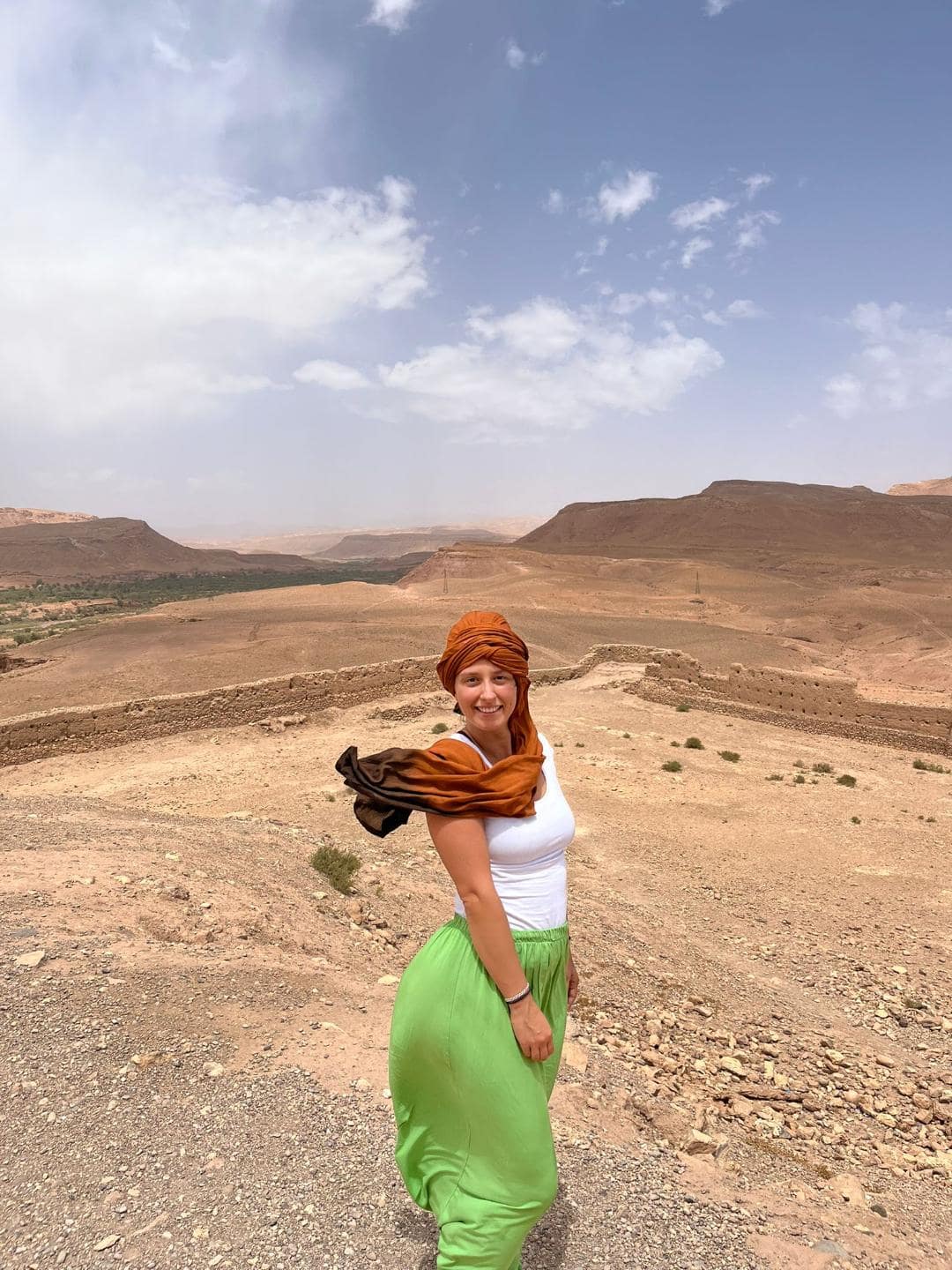 Usmiate dievča uprostred marockej púšte. Je zahalená v šatke a fúka vietor.