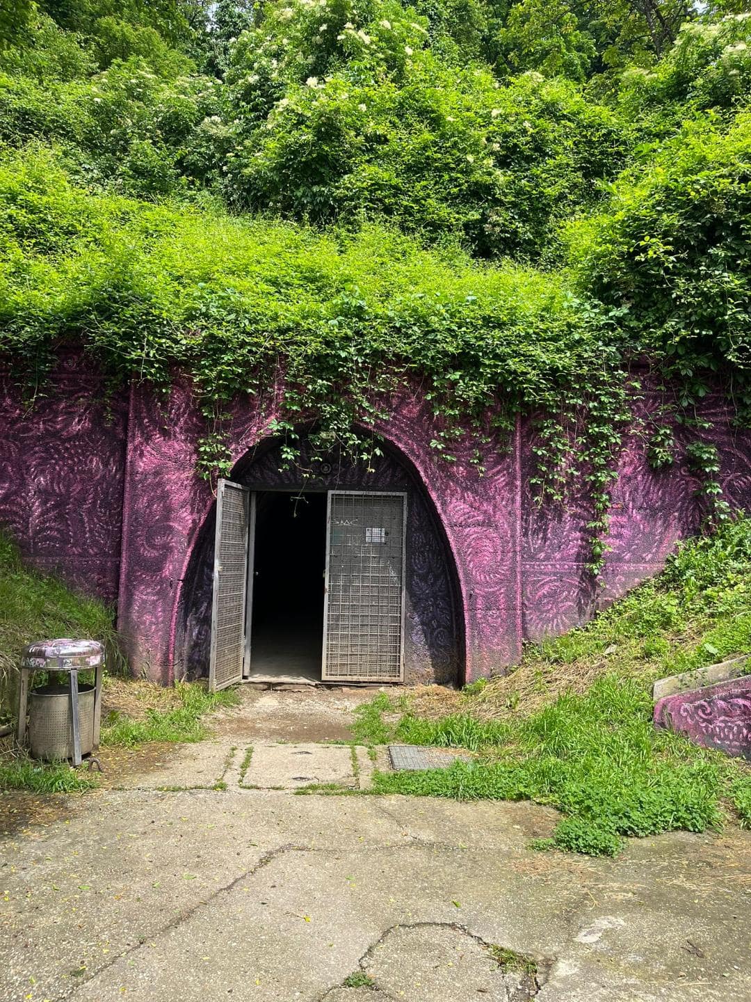 Vchod do tunela Grič v Záhrebe. Brána je vymaľovaná na fialovo a okolo nej sú rastlinné porasty.
