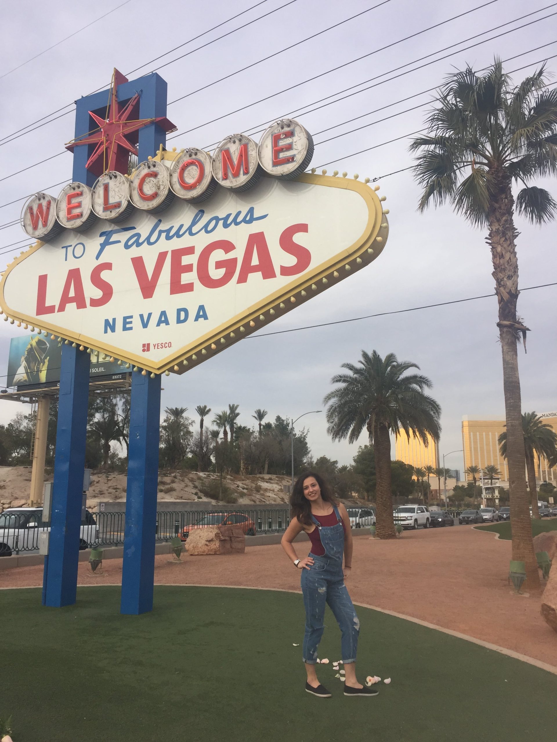 Dievča v modrom overale pózuje pred tabuľou Welcome to Fabulous Las Vegas.