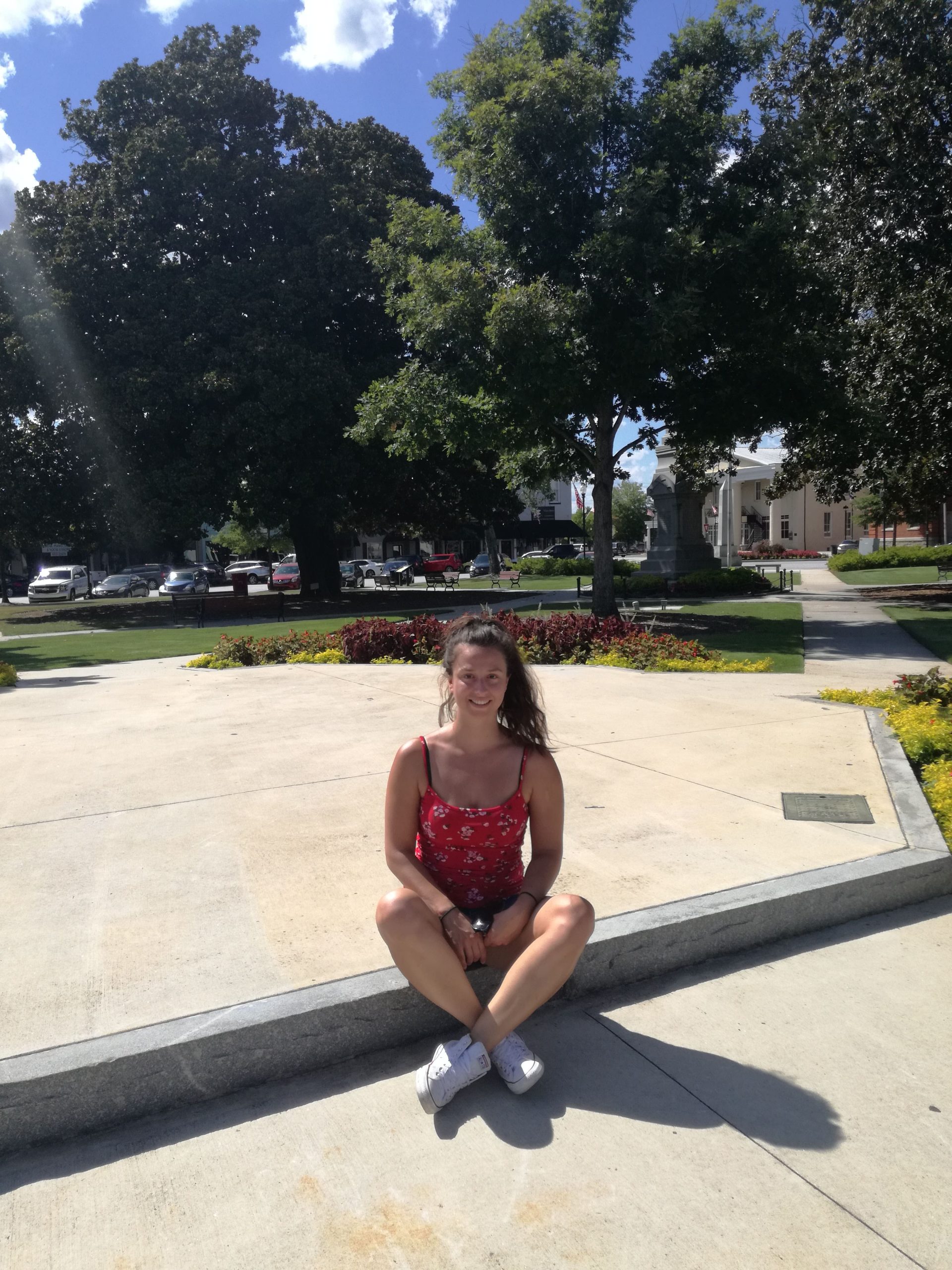 Dievča sedí na chodníku v mestskom parku a usmieva sa.