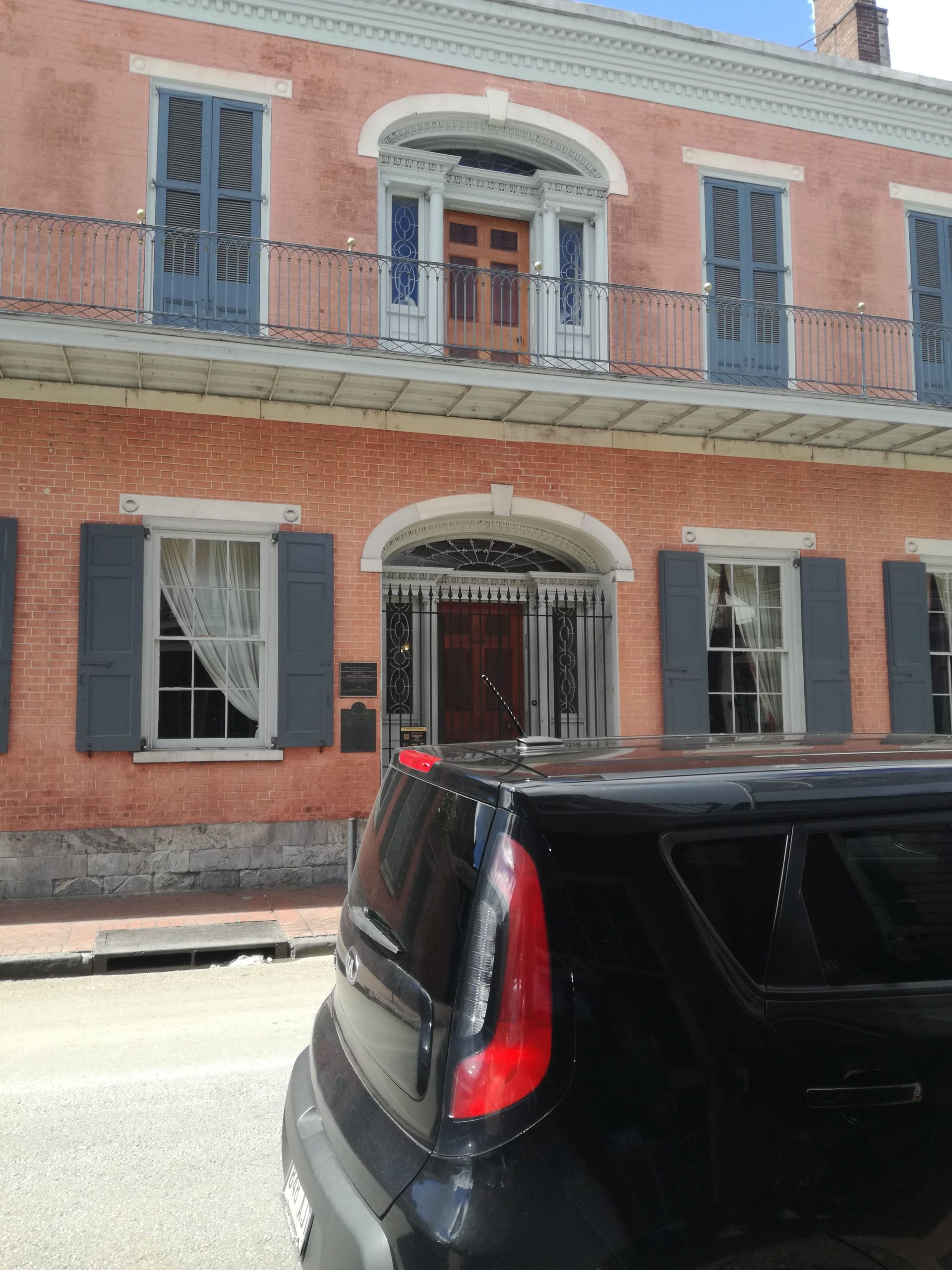 Lososový dom s krásnymi balkónmi a okenicami, pred ktorým stojí čierne auto.