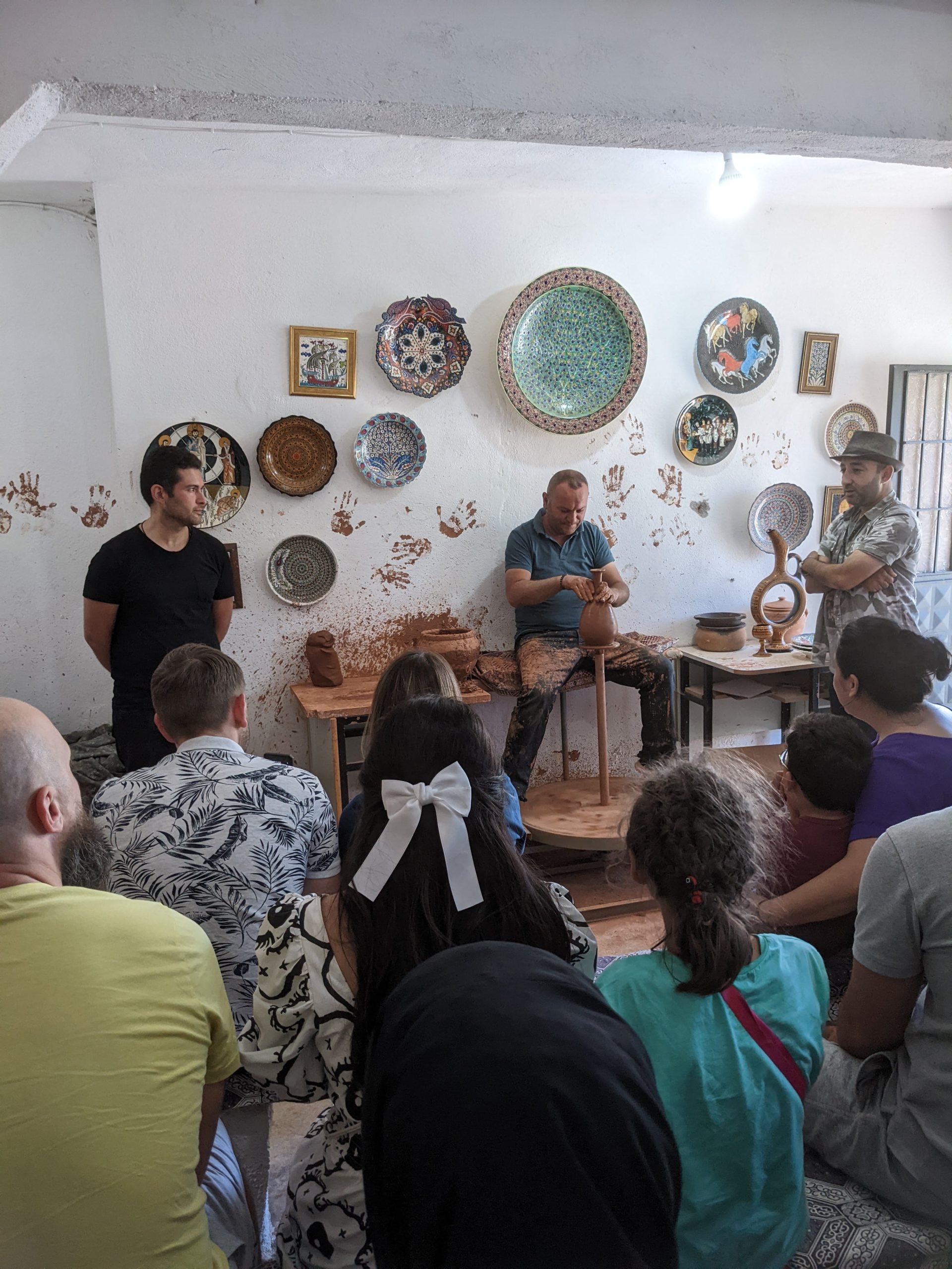 Chlap vysvetľuje publikum ako sa vyrábajú vázy na hrnčiarskom kruhu. Za ním je vidno tureckú keramiku.