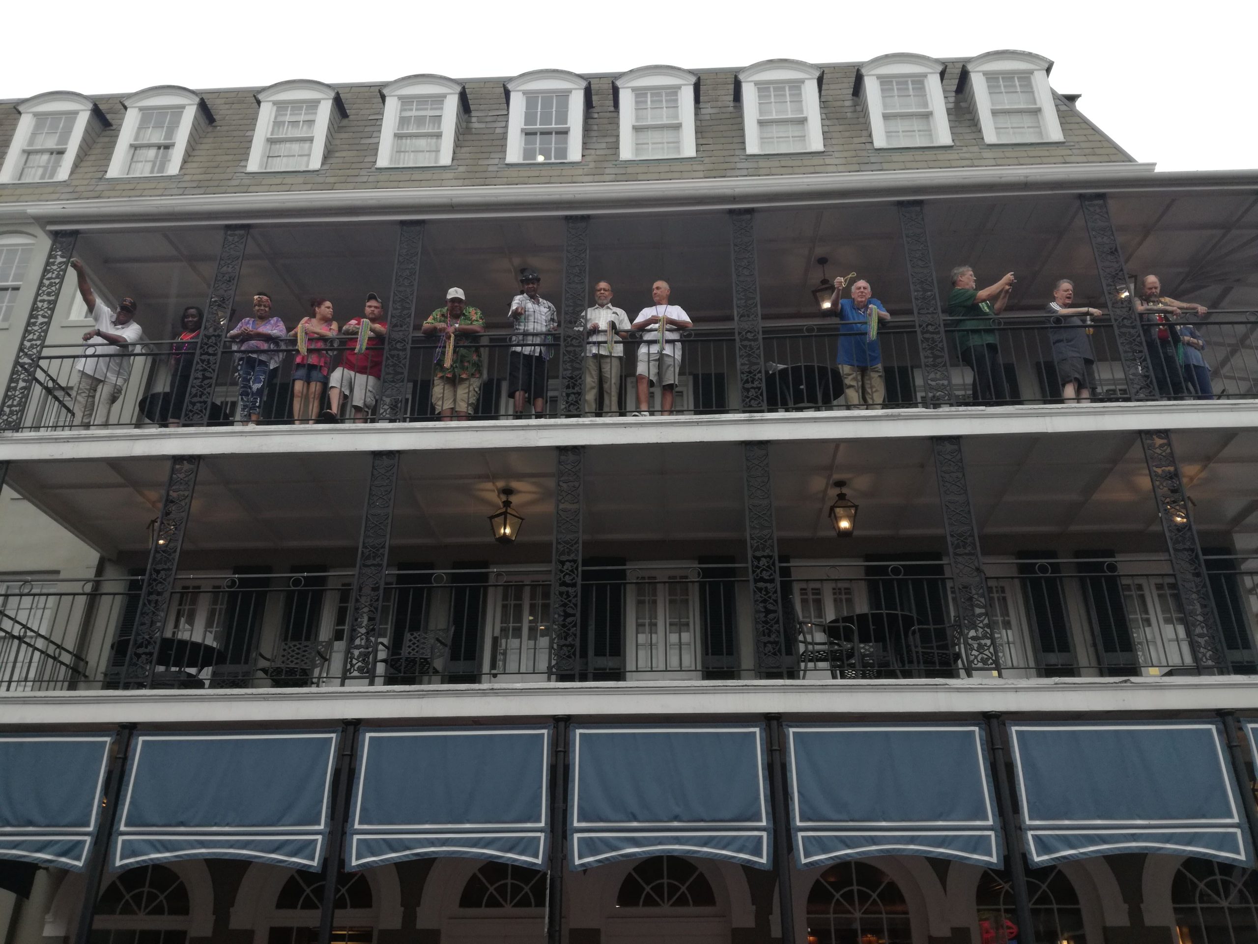 Chlapi s farebnými náhrdelníkmi v rukách stoja na balkóne.