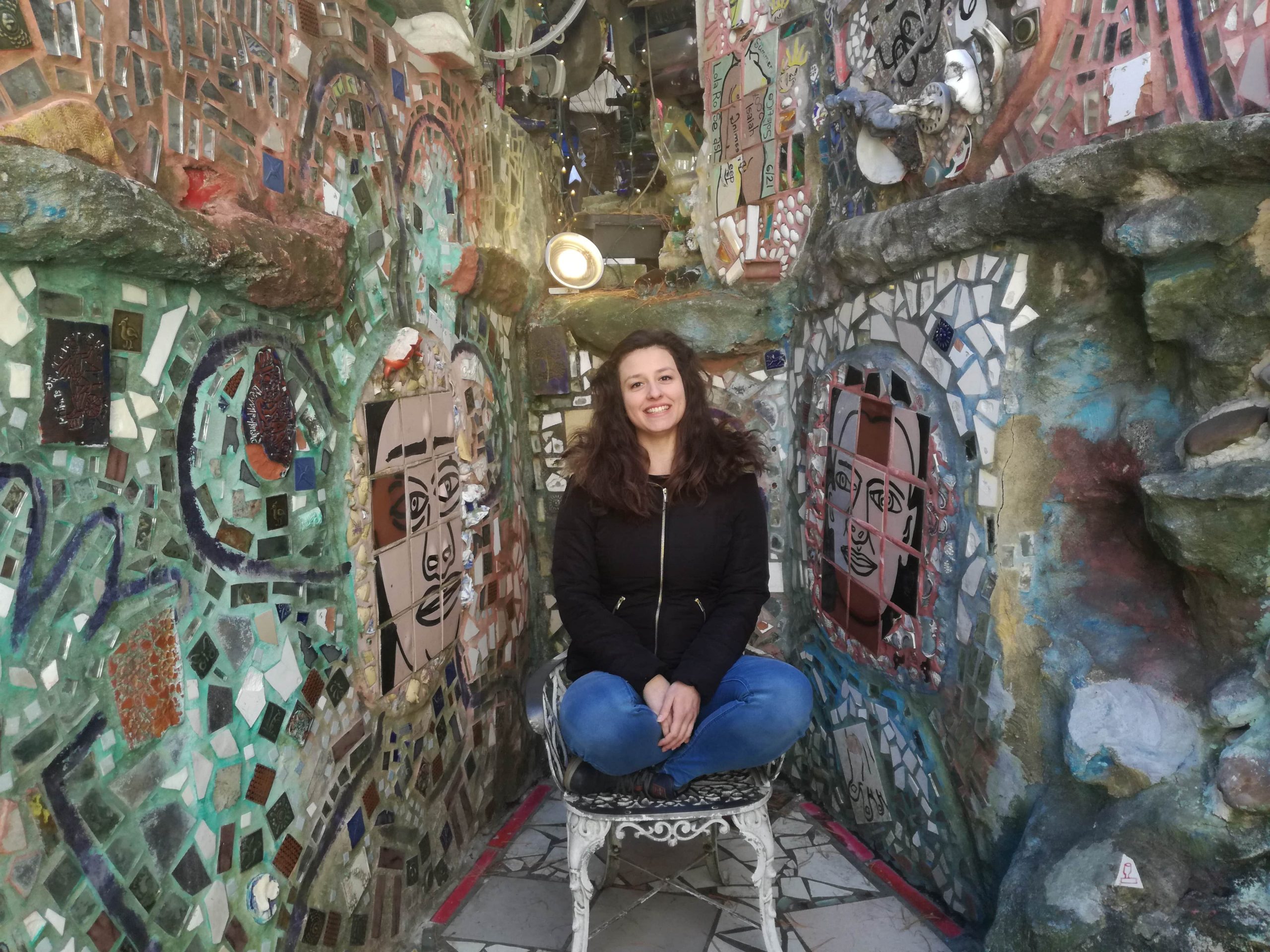 Dievča sedí na stoličke a okolo nej sú steny z farebnej mozaiky.