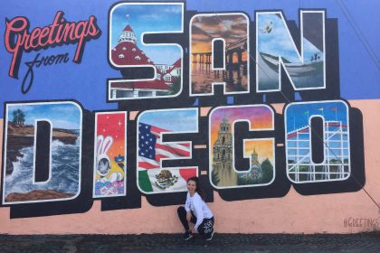 Dievča čupí pred farebným nápisom Greetings from San Diego.