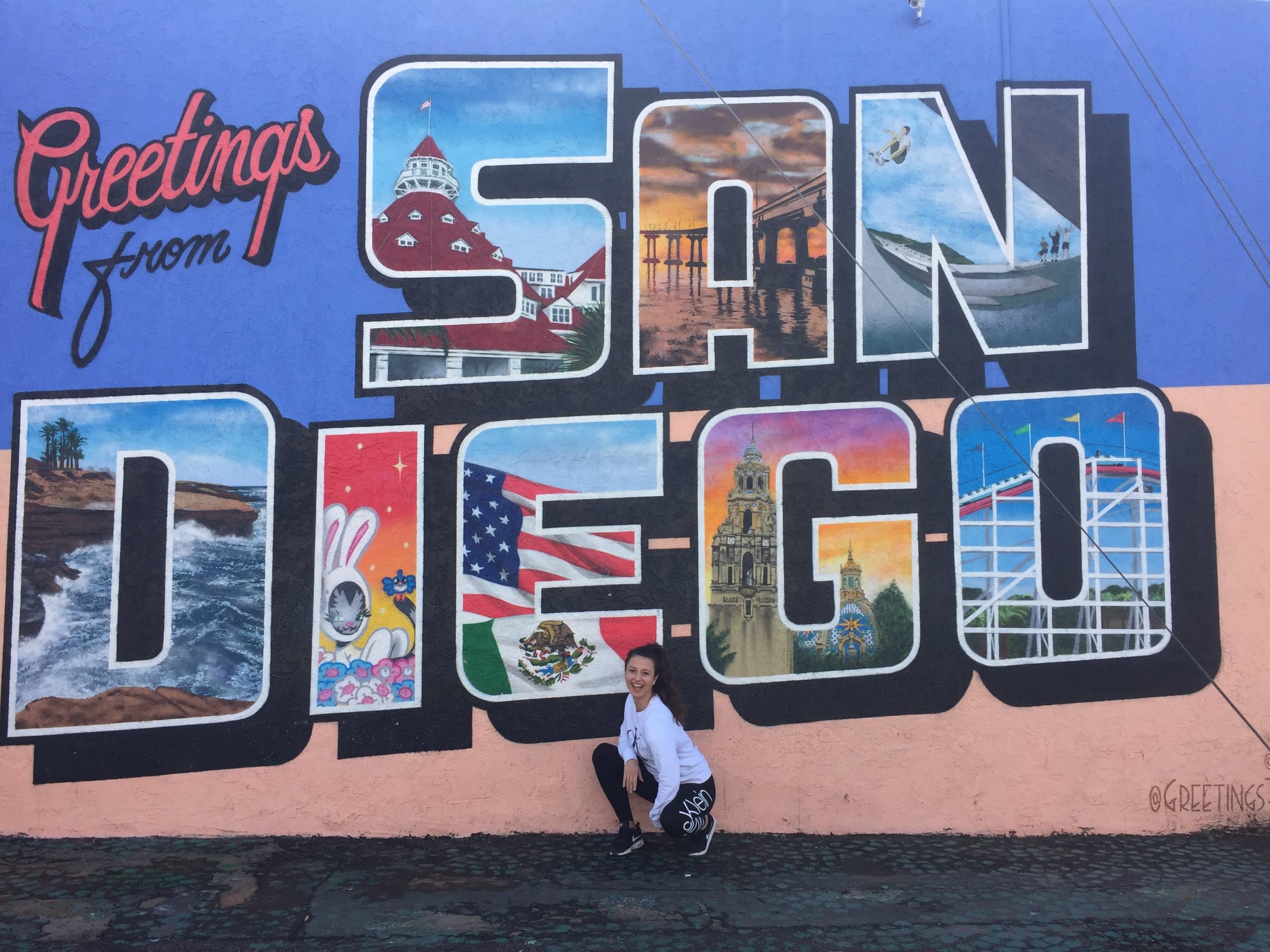 Dievča čupí pred farebným nápisom Greetings from San Diego.