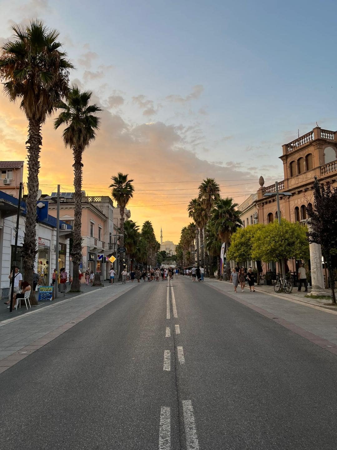 Hlavná ulica s vysokými palmami počas západu slnka.