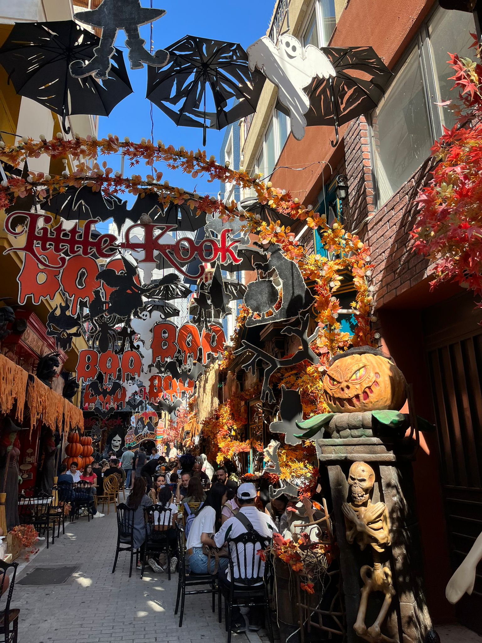Ulica dekorovaná do Halloween tématiky. Sú tam tekvice, zombie, duchovia a turisti na stoličkách.