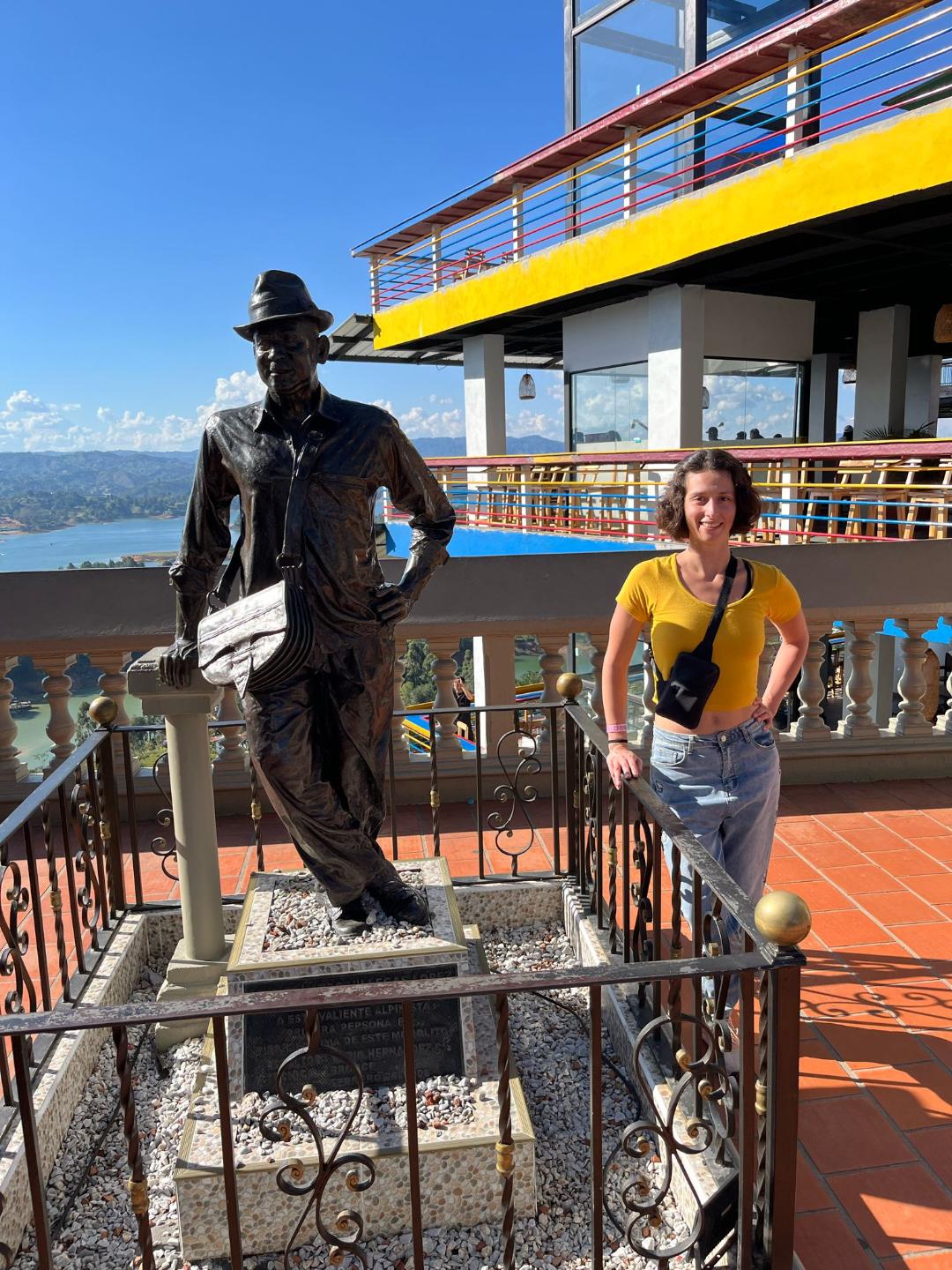 Dievča v žltom tričku stojí vedľa sochy chlapa.