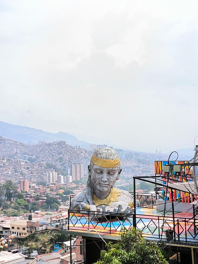 Gigantická socha mužskej hlavy, ktorá pred sebou drží dlane. Za ňou je panoramatický výhľad na mesto.