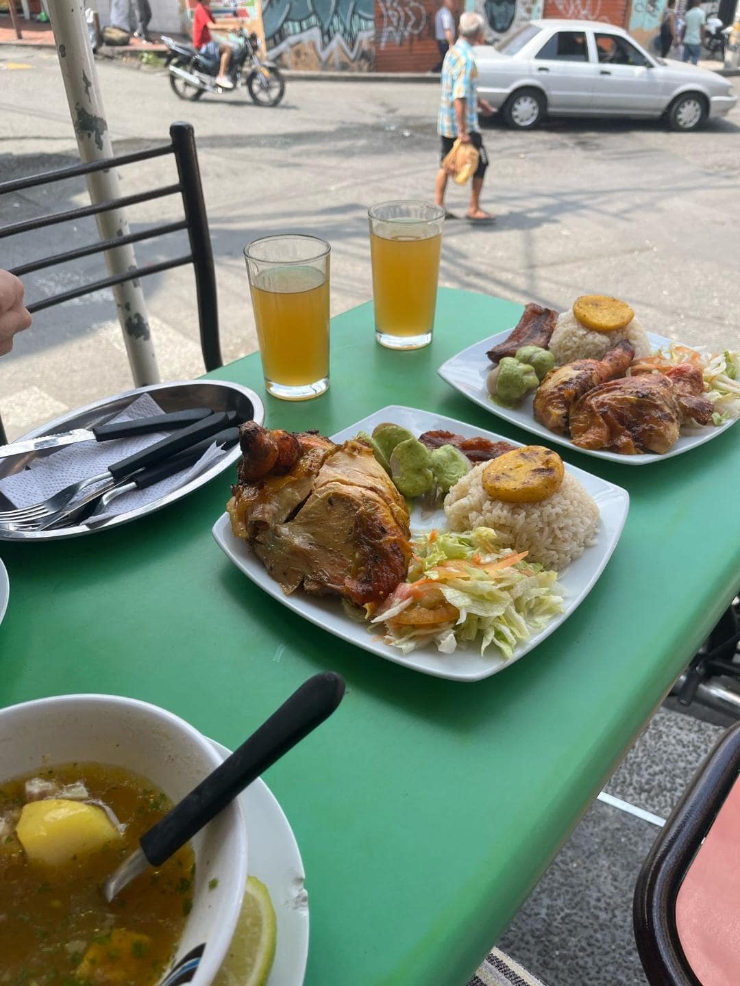 Na stole je hlavné jedlo kuracie prsia s ryžou a zeleninou a polievka. Sú tam aj dva oranžové nápoje.