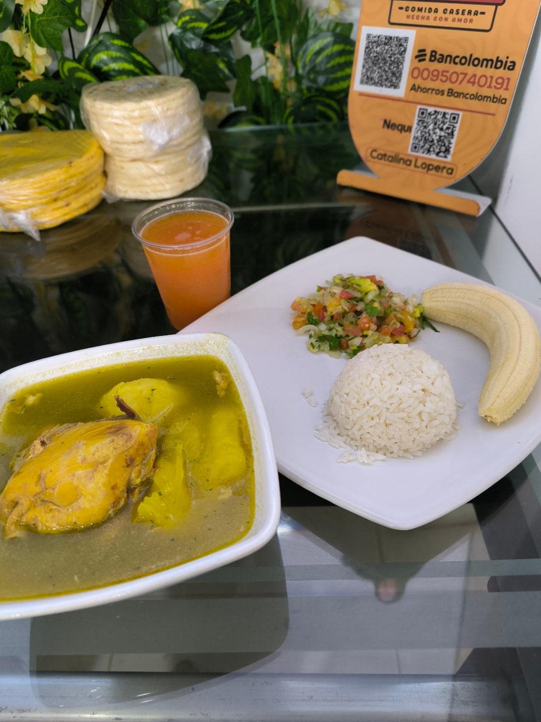 Kuracia polievka s tanierom ryže, zeleninou a banánom. Za taniermi je sladký nápoj.