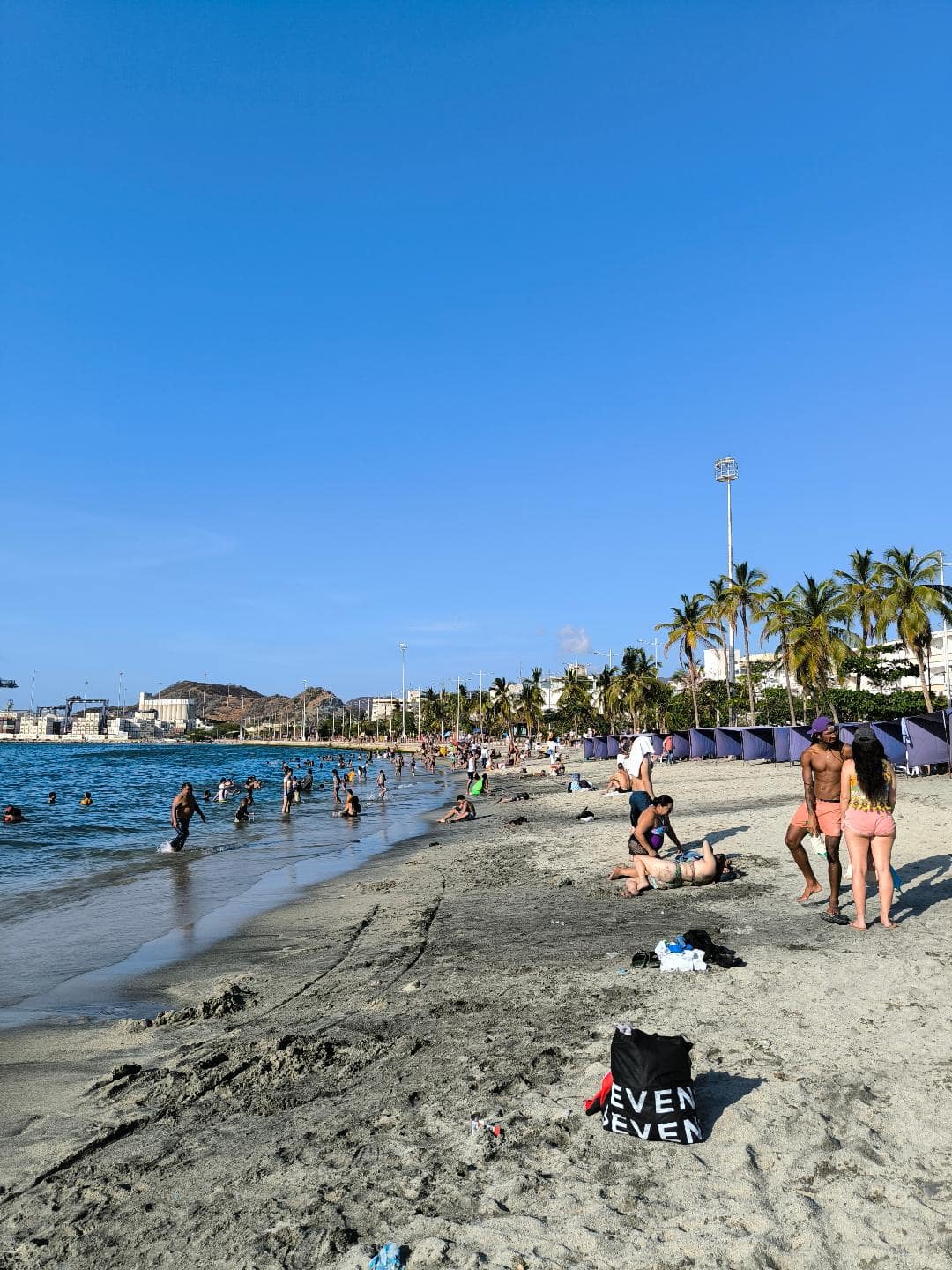 Pláž, more, palmy a relaxujúci turisti.