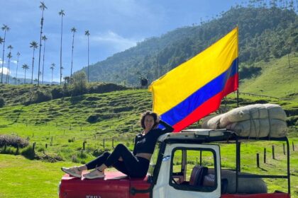 Dievča sedí na kapote červeného jeepu. Za ňou veje kolumbijská vlajka.