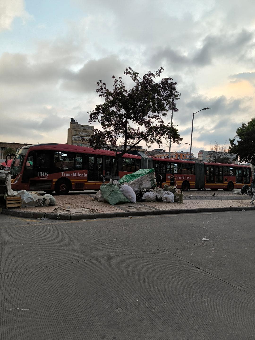 Červený autobus jazdí počas západu slnka. Vedľa neho sú na zemi hodené odpadky.