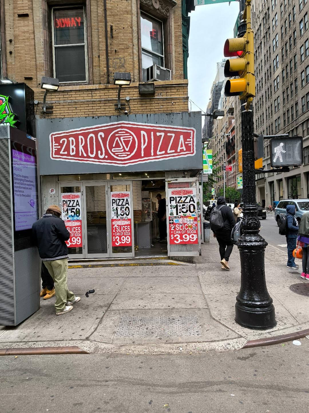 Sivá budova pizzerie v New Yorku. Je na nej nápis 2 Bros Pizza.