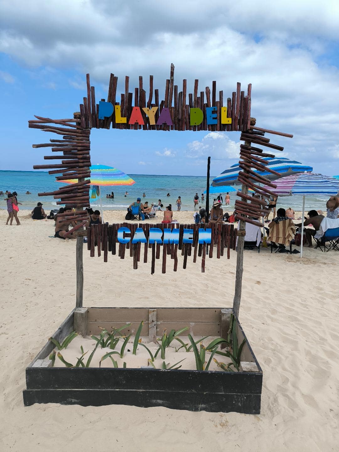 Tabuľa na piesočnatej pláži, na ktorej je farebný nápis Playa del Carmen.