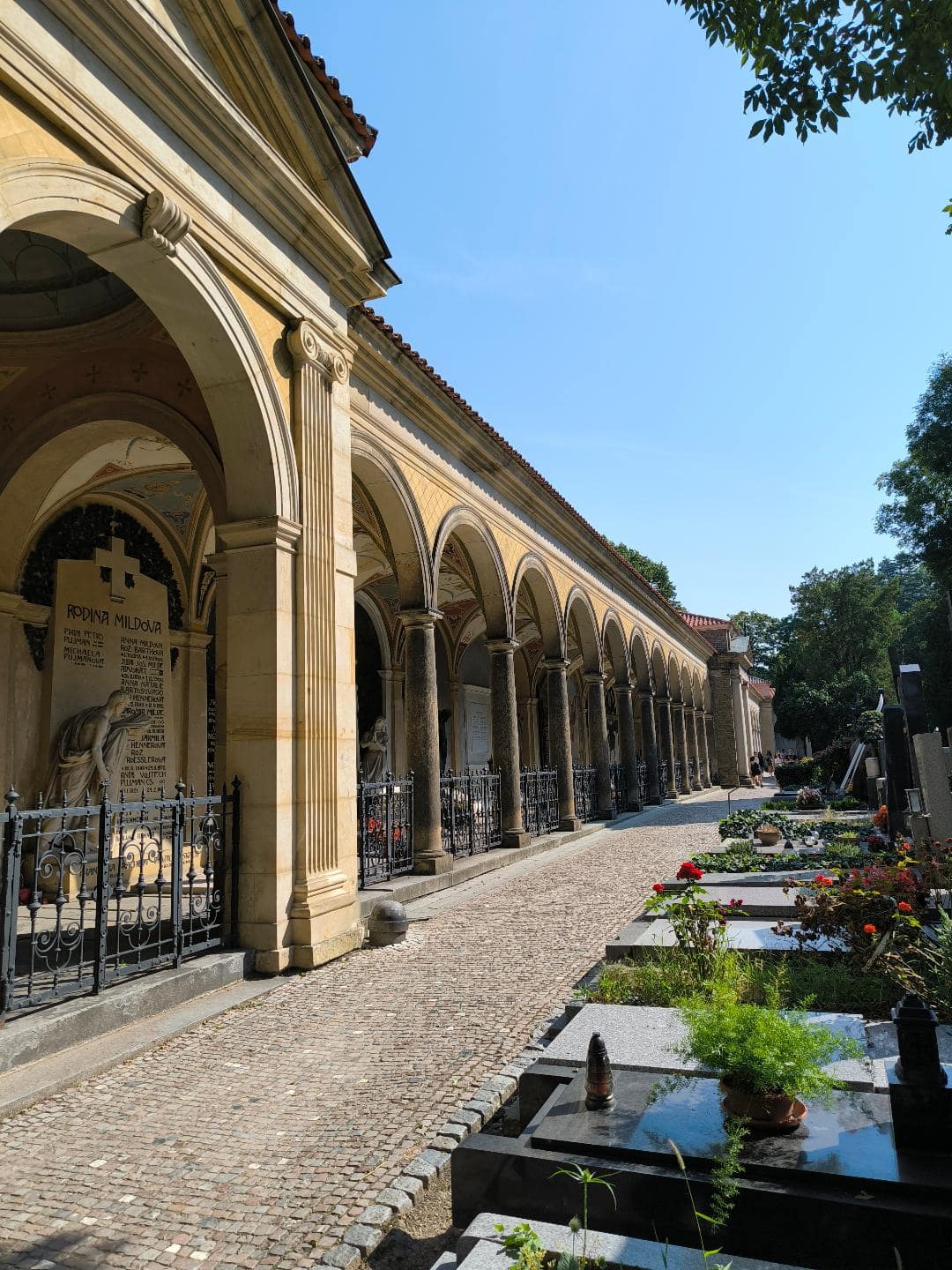 Chodník, ktorý vedie cez cintorín. Na jednej strane sú hroby a na druhej strane je oblúkovité stĺporadie.