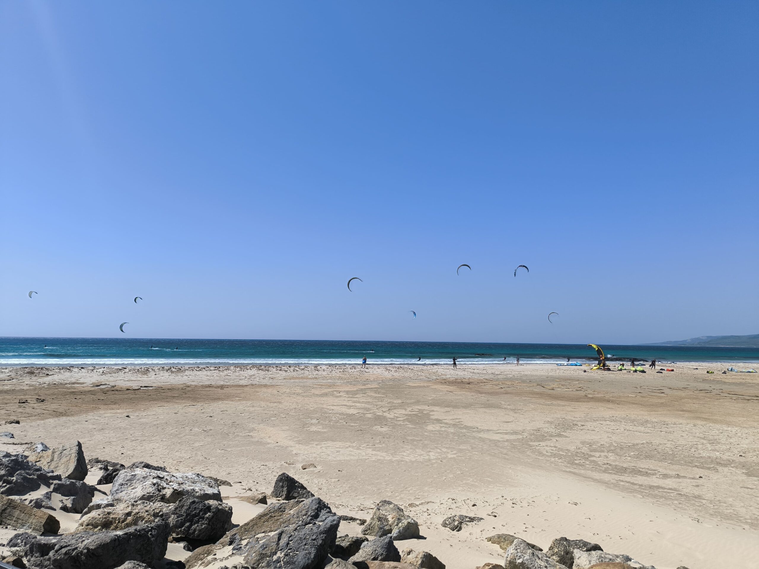 Mestská piesočnatá pláž. V mori za plážou lietajú kitesurferi.