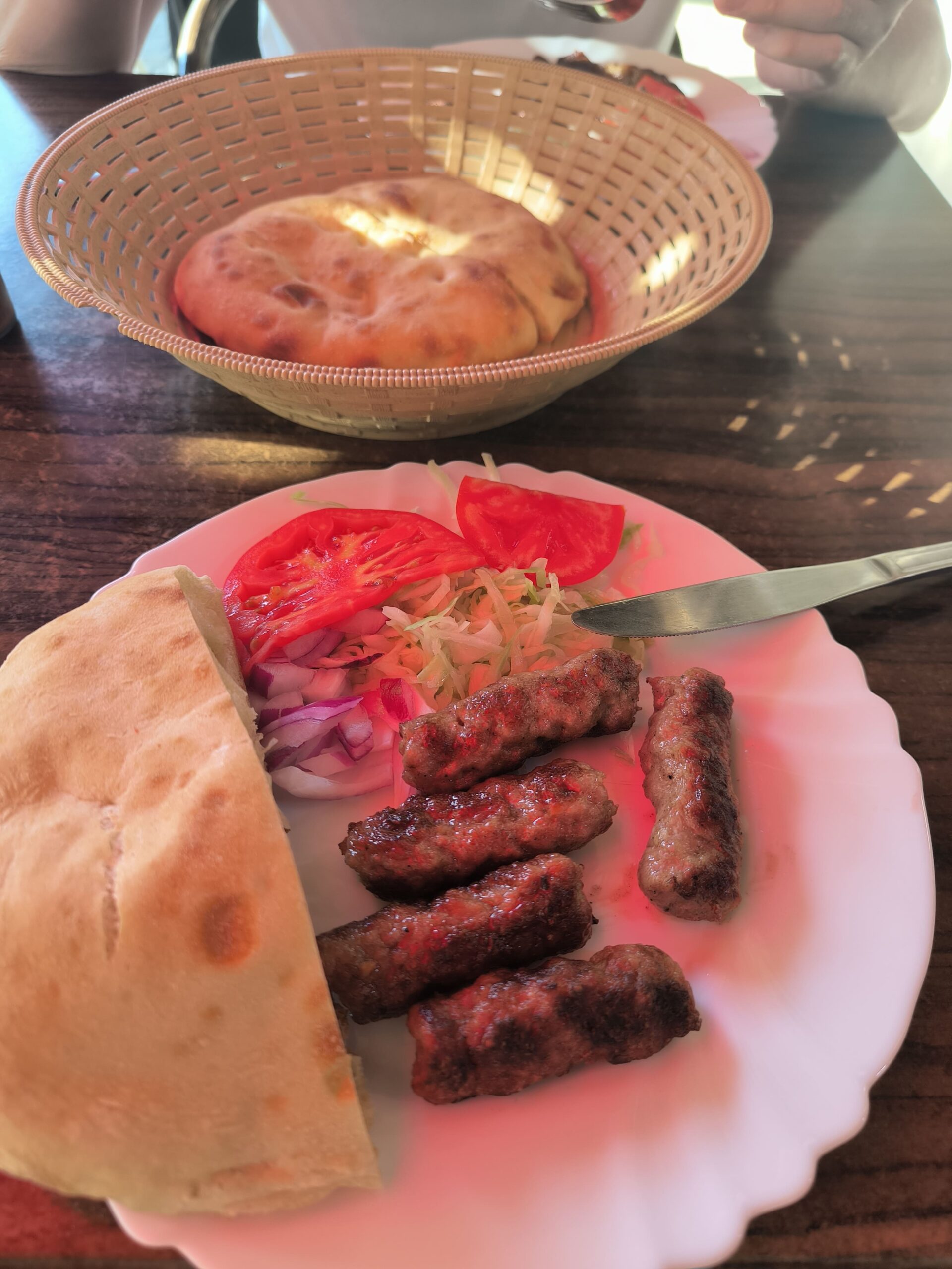 Na tanieri sú valčeky z mletého mäsa, paradajka, cibuľa a pita placka.