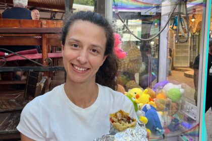 Dievča v bielom tričku sedí v reštaurácií a v ruke drží kebab.