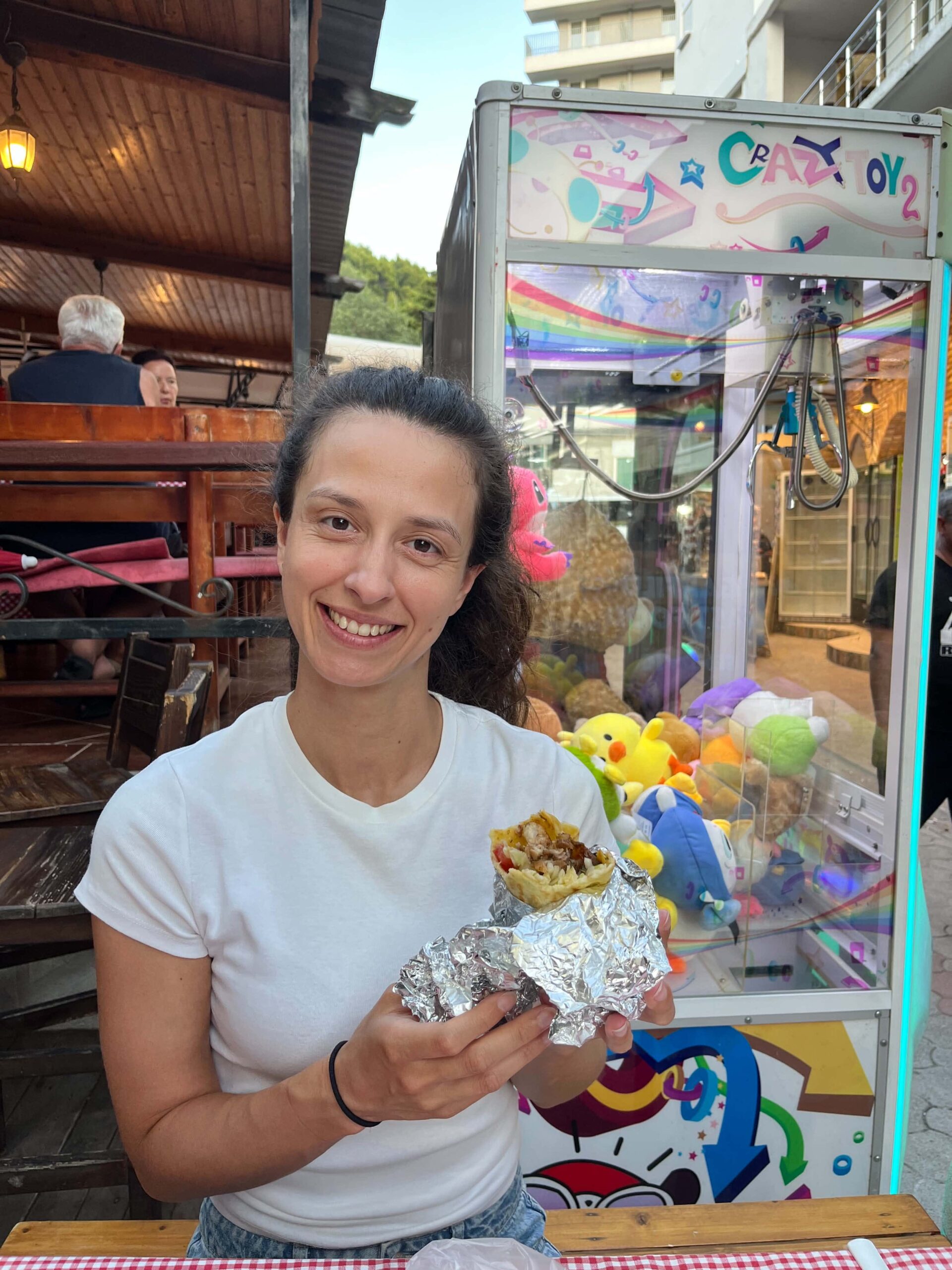 Dievča v bielom tričku sedí v reštaurácií a v ruke drží kebab.